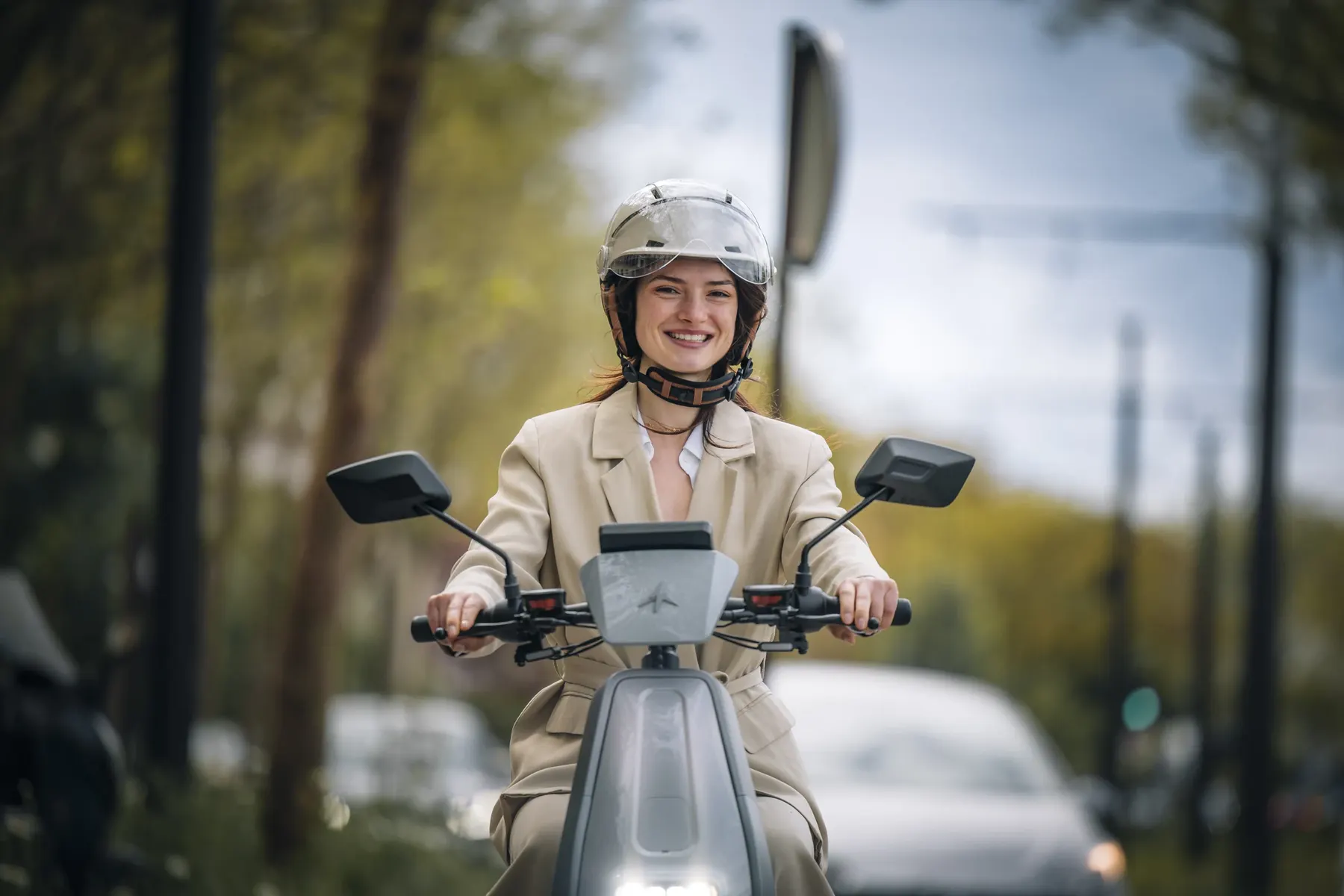 Une femme en tailleur beige sourit au guidon de son KICK K2 Hillstorm, de face