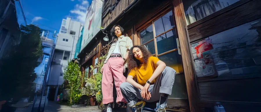 Deux jeunes posent devant une façade en bois dans une ruelle, l'un porte une montre Echo Rainbow GPS