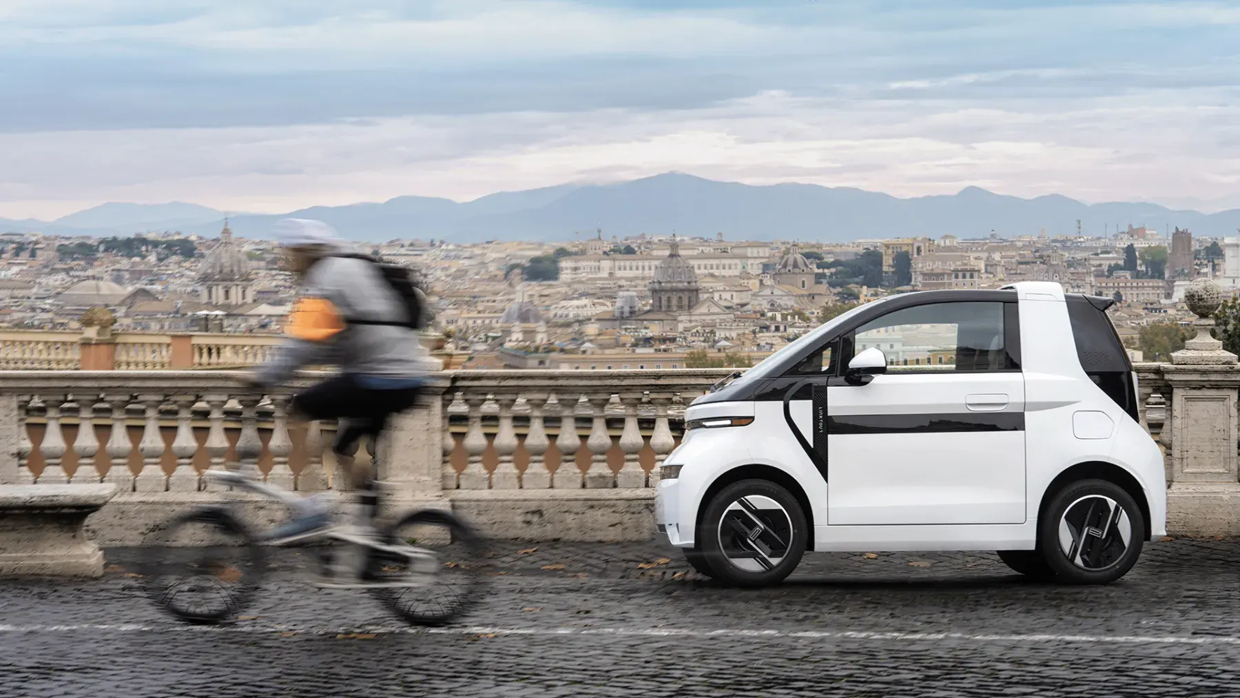 Voiture électrique Linktour Alumi blanche dans une rue, un cycliste passe devant