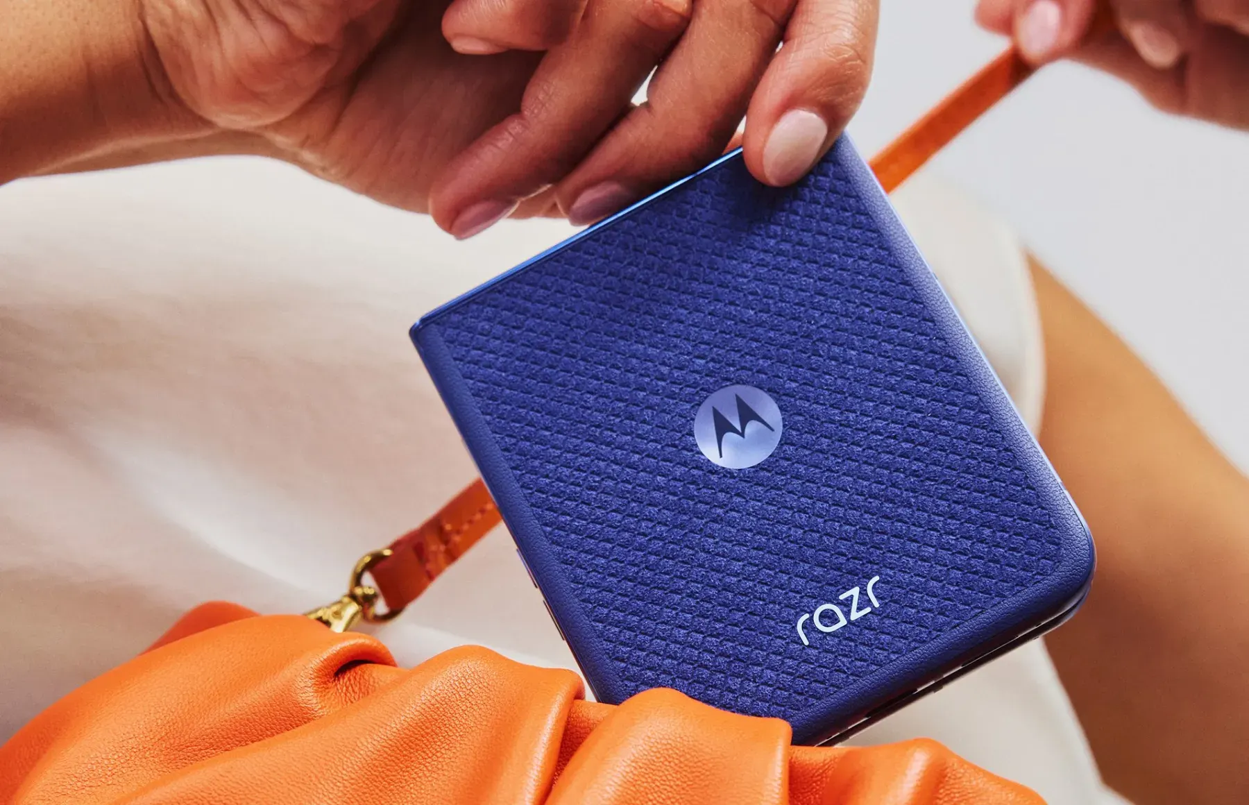 Smartphone pliant razr bleu tenu fermé au-dessus d'un sac orange