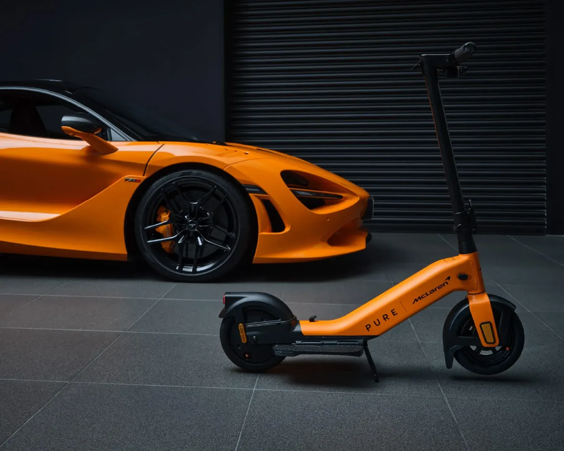Trottinette Pure x McLaren orange à côté d'une voiture de sport McLaren
