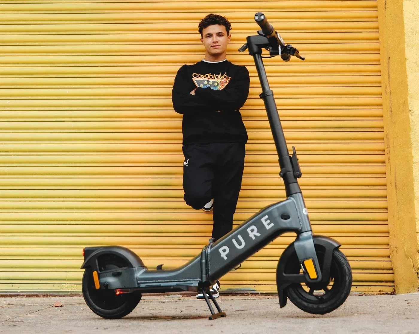 Homme appuyé contre un mur jaune à côté d'une trottinette Pure Electric