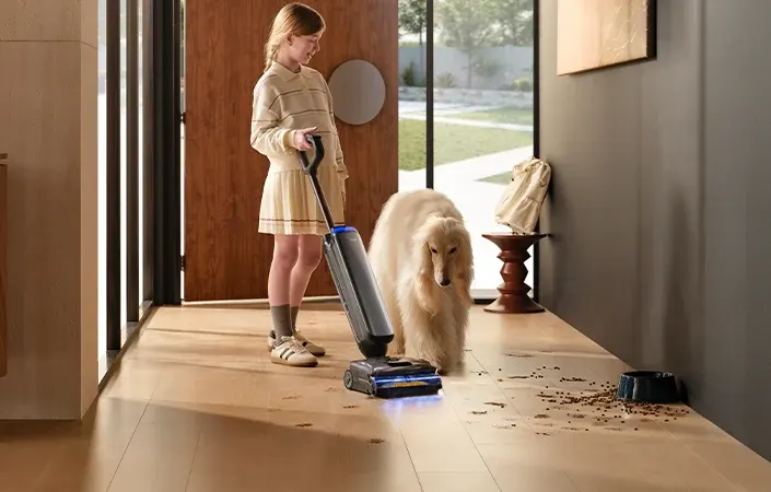 Petite fille passant un aspirateur laveur Tineco dans une entrée, à côté d'un chien